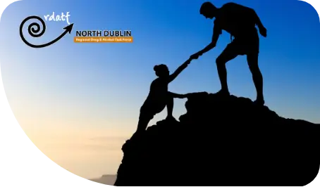 Silhouette of one person helping another climb a rock against a twilight sky.