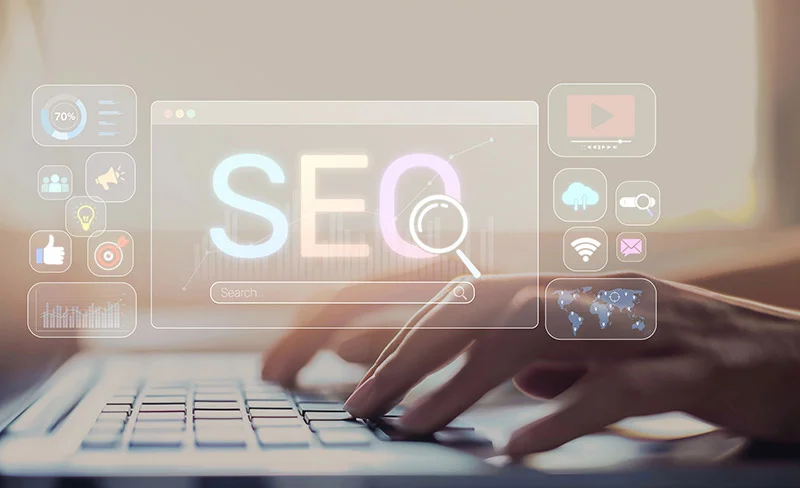 Close-up of hands typing on a laptop with a translucent SEO dashboard overlay and a magnifying glass over the letters SEO.
